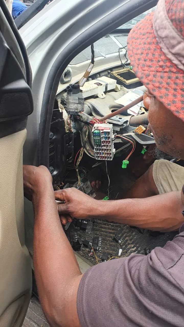ONYEBEST technician working on a wiring loom and fuse box behind a Volvo dashboard in Mushin, Lagos